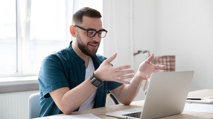 Millennial Caucasian male worker in glasses have video call on laptop in office, smiling young man employee talk speak engaged in online conference using computer gadget, communication concept