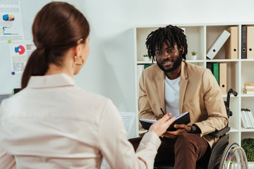 Selective focus of recruiter and african american disabled employee with copybook looking at each other at job interview