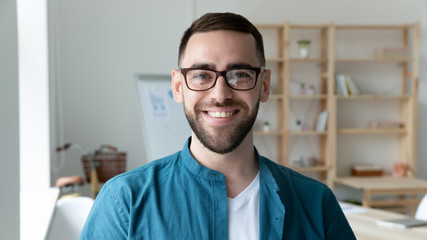 headshot portrait of smiling caucasian young man ceo or boss in glasses posing in modern office, hap