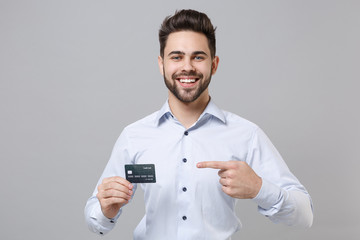 Canvas Print - Smiling young unshaven business man in light shirt posing isolated on grey background in studio. Achievement career wealth business concept. Mock up copy space. Point index finger on credit bank card.