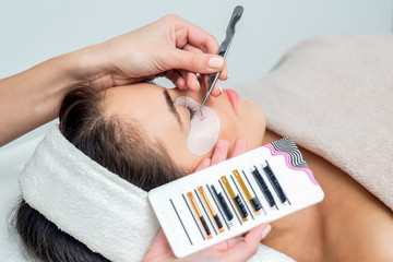 Wall Mural - Young woman receiving eyelash extension procedure in beauty salon.