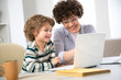 © chagin - Business woman and her cute little son are using a laptop and smiling while sitting in home office
