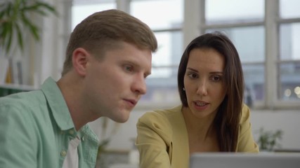 Wall Mural - Zoom in medium shot of young man and woman looking at laptop screen and arguing while discussing project at office