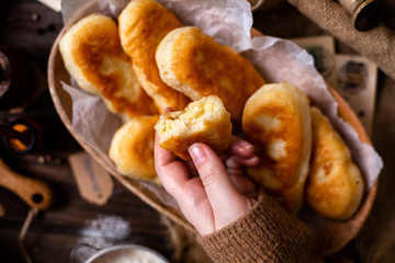 fried russian or ukrainian mini pies in oval wooden dish on rustic table with onion, pepper, flour