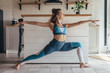 © undrey - Young fit woman exercising at home doing warrior pose.