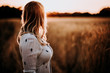 woman from behind standing in wheat field while sunset. Copy space