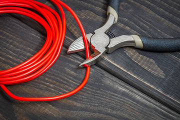 The electrician pliers and red wire on black wooden boards for repairing energized systems or communications