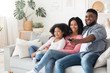© Prostock-studio - Smiling african american family relaxing and watching tv in living room