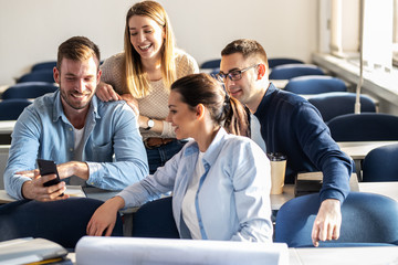 Wall Mural - College students making fun in the classroom ,using smartphone and laughing.