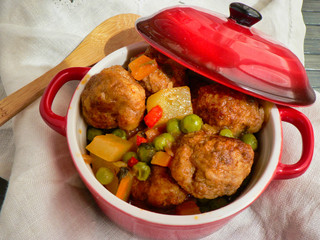 Canvas Print - Meatballs with potatoes and peas in a red casserole, wooden spoon and white tablecloth