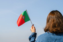 Woman Hand With Portuguese Swaying Flag On The Blue Sky. Portugal. Concept