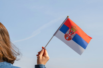 Wall Mural - Woman hand with Serbian swaying flag on the blue sky. Serbia. Concept