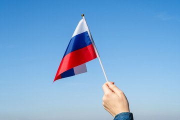 Wall Mural - Woman hand with Russian swaying flag on the blue sky. Russia. Concept