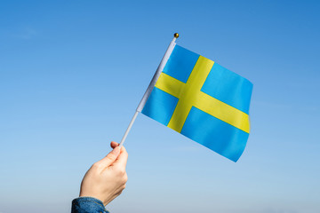 Wall Mural - Woman hand with Swedish swaying flag on the blue sky. Sweden. Concept