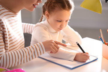 Wall Mural - Woman helping her daughter with homework at table indoors