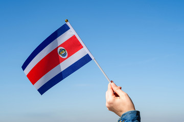 Poster - Woman hand with Costa Rica swaying flag on the blue sky. North America. Concept