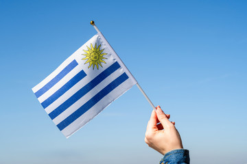 Wall Mural - Woman hand with Uruguay swaying flag on the blue sky. South America. Concept