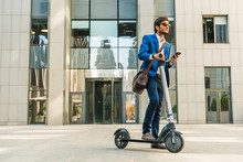 Businessman Using Cellphone While Driving Electric Scooter Near Business Center On City Street