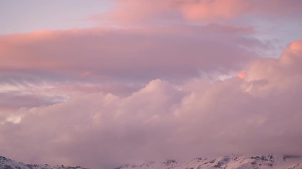 Wall Mural - Time lapse of pink clouds over mountain top at sunset as they roll over the peaks.