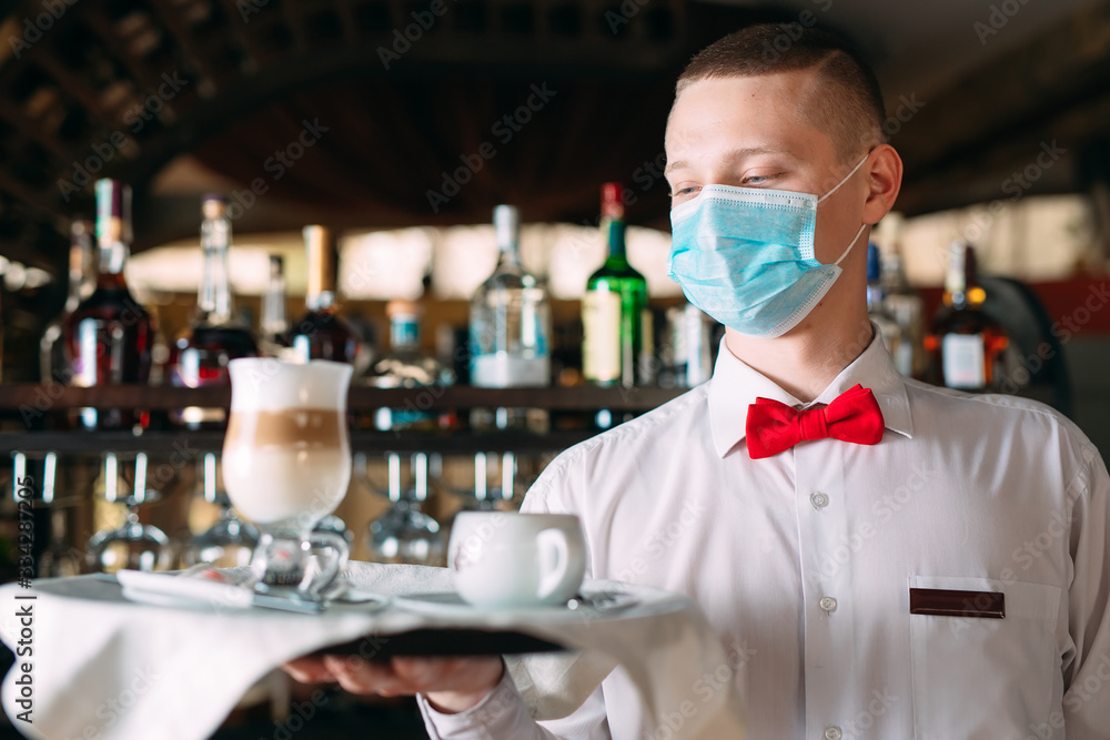 A European-looking waiter in a medical mask serves Latte coffee. - obrazy, fototapety, plakaty 
