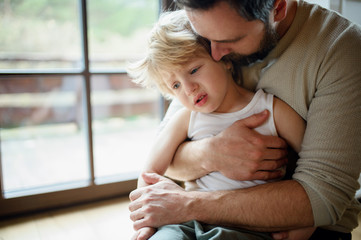 Wall Mural - Father with small sick unhappy son indoors at home, comforting him.