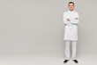 Young handsome doctor in white medical coat in full length posing on grey background, isolated with copy space for your text. Concept of healthcare and medicine advertisement