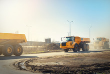 Many Big Articulated Heavy Industrial Yellow Dumper Trucks Driving On New Highway Road Construction Site On Sunny Day With Blue Sky Background. Construction Equipment Machinery Working On Open Pit