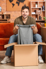 Sticker - Young man unpacking box with new clothes at home