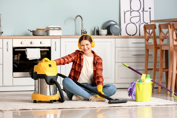 Canvas Print - Young woman listening to music while hoovering floor in kitchen