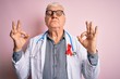 © Krakenimages.com - Senior handsome hoary doctor man wearing stethoscope and red HIV ribbon on coat relax and smiling with eyes closed doing meditation gesture with fingers. Yoga concept.