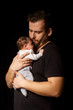 a bearded father in a black t-shirt holds a newborn baby. Dad kisses and hugs daughter or son on a black background