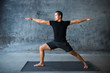 © Luna Vandoorne - Man practicing yoga in front of a dark background. Pose is warrior II, Virabhadrasana.