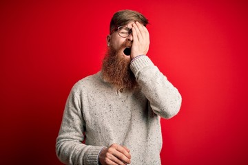 Canvas Print - Handsome Irish redhead man with beard wearing casual sweater and glasses over red background Yawning tired covering half face, eye and mouth with hand. Face hurts in pain.