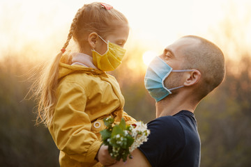 Family protection. A young father hugs his little girl daughter in the spring garden outdoors. Protective masks on faces from coronavirus infection