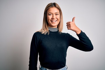 Young beautiful blonde woman with blue eyes standing over white isolated background doing happy thumbs up gesture with hand. Approving expression looking at the camera showing success.