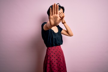 Poster - Young beautiful asian girl wearing casual dress standing over isolated pink background covering eyes with hands and doing stop gesture with sad and fear expression. Embarrassed and negative concept.