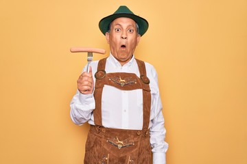 Canvas Print - Senior grey-haired man wearing german traditional octoberfest suit holding fork with sausage scared in shock with a surprise face, afraid and excited with fear expression