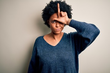 Wall Mural - Young beautiful African American afro woman with curly hair wearing casual sweater making fun of people with fingers on forehead doing loser gesture mocking and insulting.