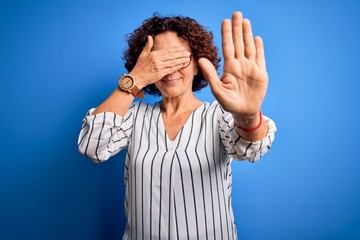 Poster - Middle age beautiful curly hair woman wearing casual striped shirt over isolated background covering eyes with hands and doing stop gesture with sad and fear expression. Embarrassed and negative