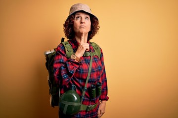 Poster - Middle age curly hair hiker woman hiking wearing backpack and water canteen using binoculars Thinking concentrated about doubt with finger on chin and looking up wondering