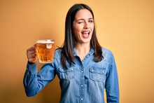 Young Woman With Blue Eyes Drinking Jar Of Beer Standing Over Isolated Yellow Background Winking Looking At The Camera With Sexy Expression, Cheerful And Happy Face.