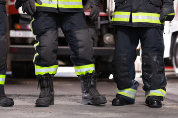 Wall Mural - Abstract professional firefighters wearing uniforms and protective helmets. Firetruck in the background.