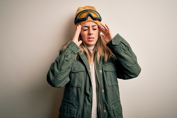 Sticker - Young brunette skier woman wearing snow clothes and ski goggles over white background with hand on headache because stress. Suffering migraine.