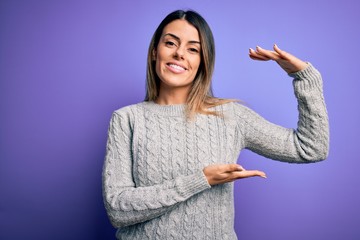 Sticker - Young beautiful woman wearing casual sweater standing over isolated purple background gesturing with hands showing big and large size sign, measure symbol. Smiling looking at the camera. Measuring