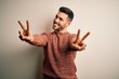 © Krakenimages.com - Young handsome man wearing casual sweater standing over isolated white background smiling with tongue out showing fingers of both hands doing victory sign. Number two.