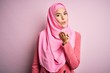 © Krakenimages.com - Young beautiful girl wearing muslim hijab standing over isolated pink background looking at the camera blowing a kiss with hand on air being lovely and sexy. Love expression.
