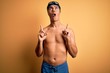 © Krakenimages.com - Young handsome man shirtless wearing swimsuit and swim cap over isolated yellow background amazed and surprised looking up and pointing with fingers and raised arms.