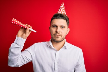 Wall Mural - Young man with blue eyes wearing birthday cap and holding festive trumpet with a confident expression on smart face thinking serious