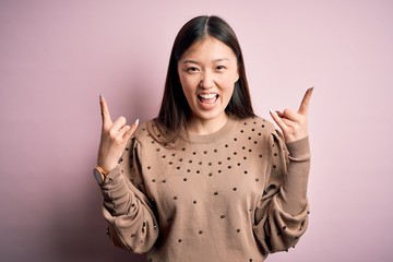 Sticker - Young beautiful asian woman wearing fashion and elegant sweater over pink solated background shouting with crazy expression doing rock symbol with hands up. Music star. Heavy music concept.