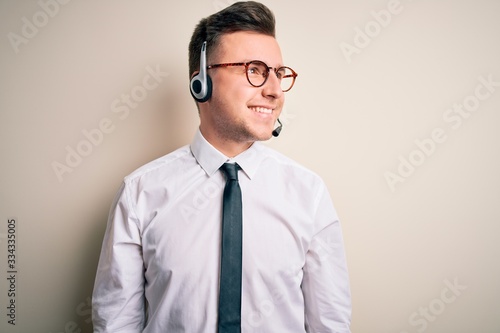 Young handsome caucasian business man wearing call center headset at customer service looking away to side with smile on face, natural expression Poster Mural XXL